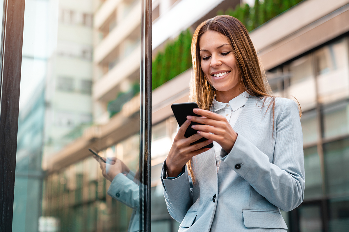 Young smiling businesswoman using mobile phone outdoors
